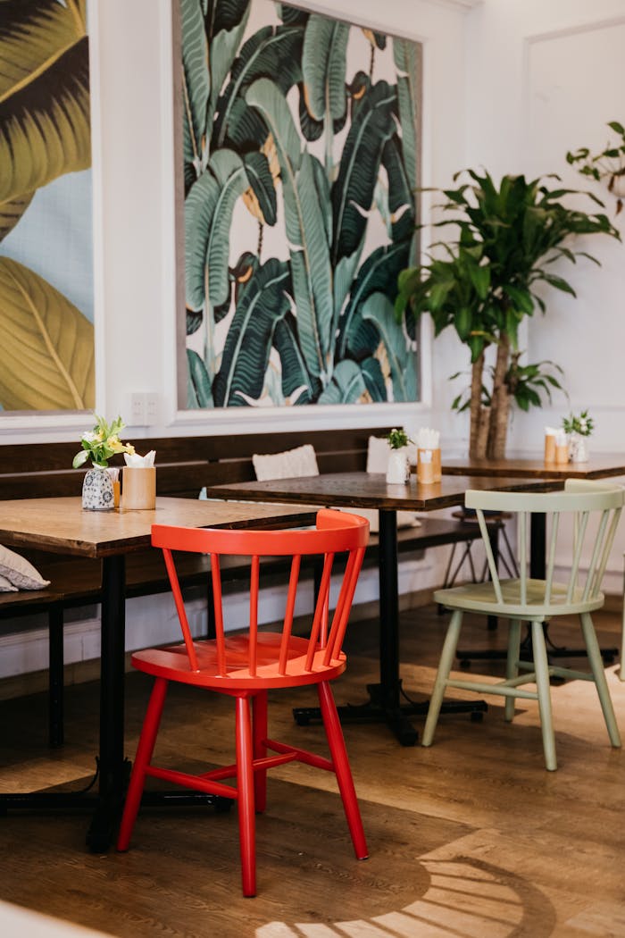Stylish cafe interior featuring vibrant red chair, lush plants, and artistic wall decor.