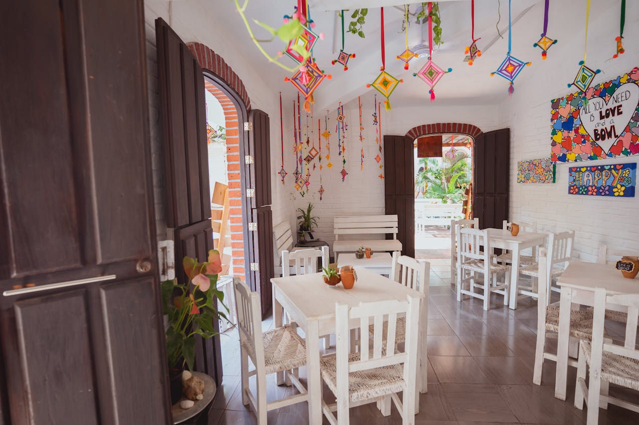 Bright cafe interior featuring colorful hanging decorations and white furniture with natural light.